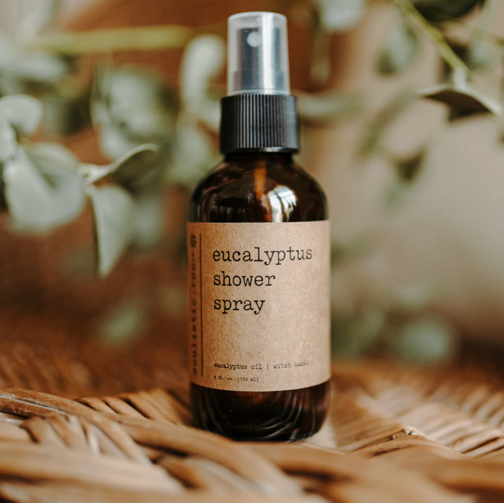 Eucalyptus shower spray bottle with a natural label on a woven surface with blurred greenery in the background.
