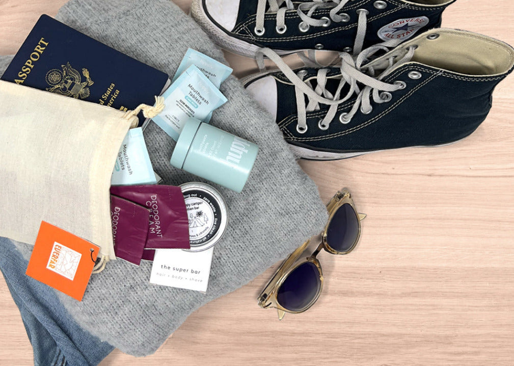 Travel essentials including shoes, passport, sunglasses, and toiletries on a wooden surface.